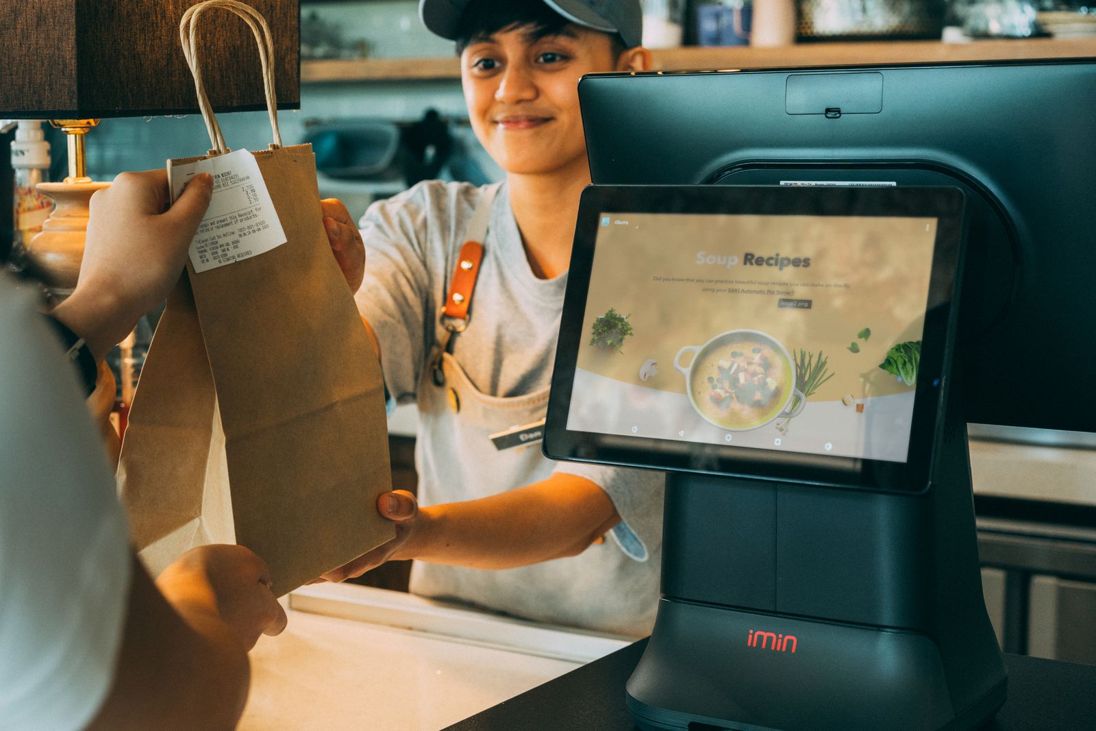 Un empleado entrega un pedido y un recibo en el mostrador de un comercio, junto a una tableta de caja